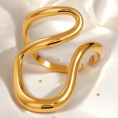 Eleganter goldfarbener Wellenring mit skulpturaler, offener Form – moderner Statement-Ring von LOÉAR auf hellem Hintergrund.