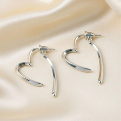 Silberne, offen geformte Herz-Ohrringe mit fließender Linienführung auf hellem Hintergrund.