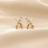 Vergoldete X-Design Ohrringe mit Perlen und Zirkonia auf satinierter Oberfläche.