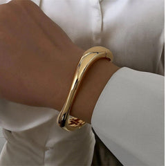 Elegantes Armband in glänzendem Goldton mit fließender, moderner Form – minimalistischer Armreif von LOÉAR, getragen am Handgelenk.