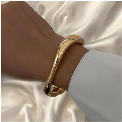 Elegantes Armband in glänzendem Goldton mit fließender, moderner Form – minimalistischer Armreif von LOÉAR, getragen am Handgelenk.