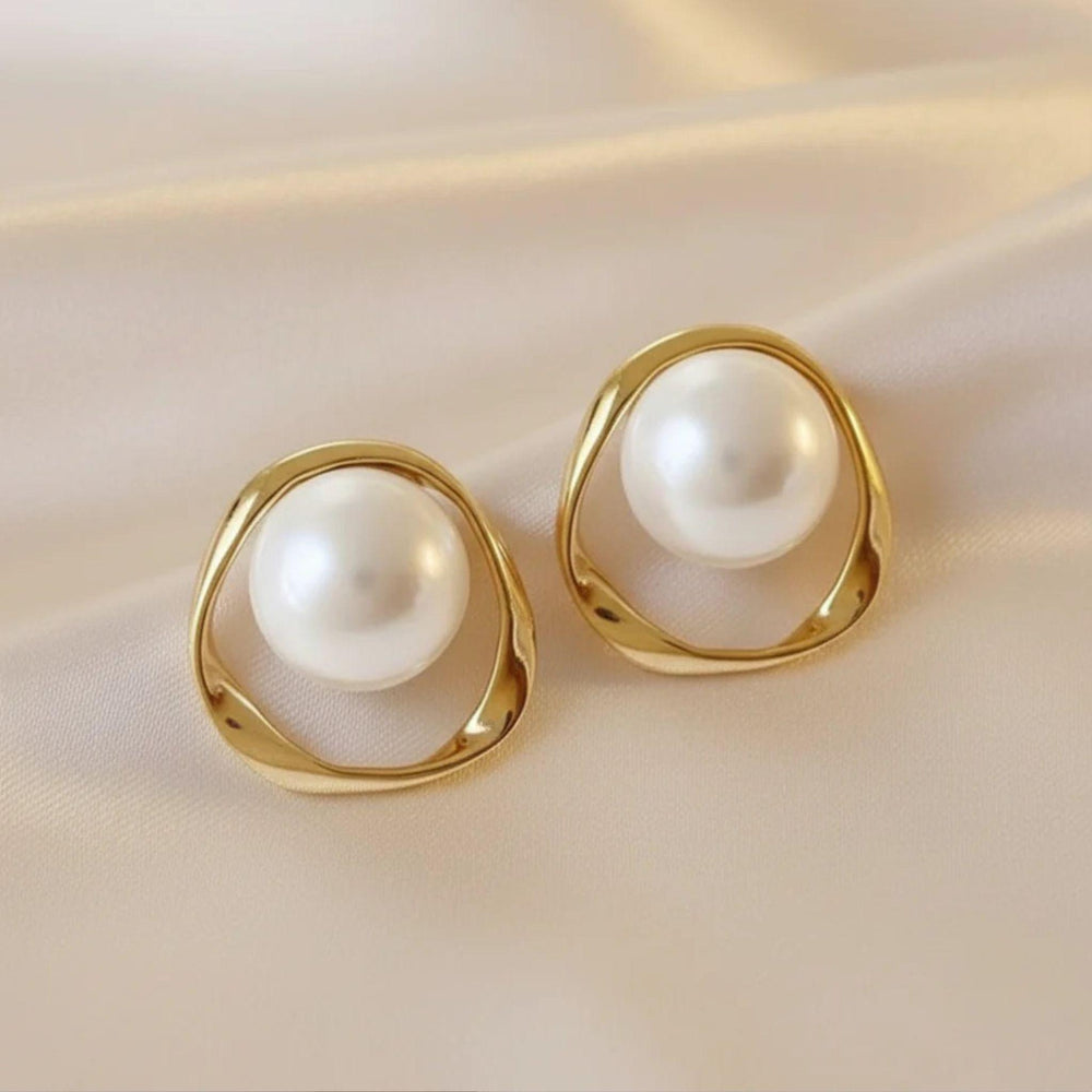 Vergoldete Ohrringe mit großer Perlenkugel und organischem Rahmen auf Satinuntergrund