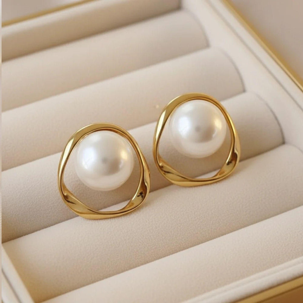 Vergoldete Ohrringe mit großer Perlenkugel und organischem Rahmen auf Satinuntergrund