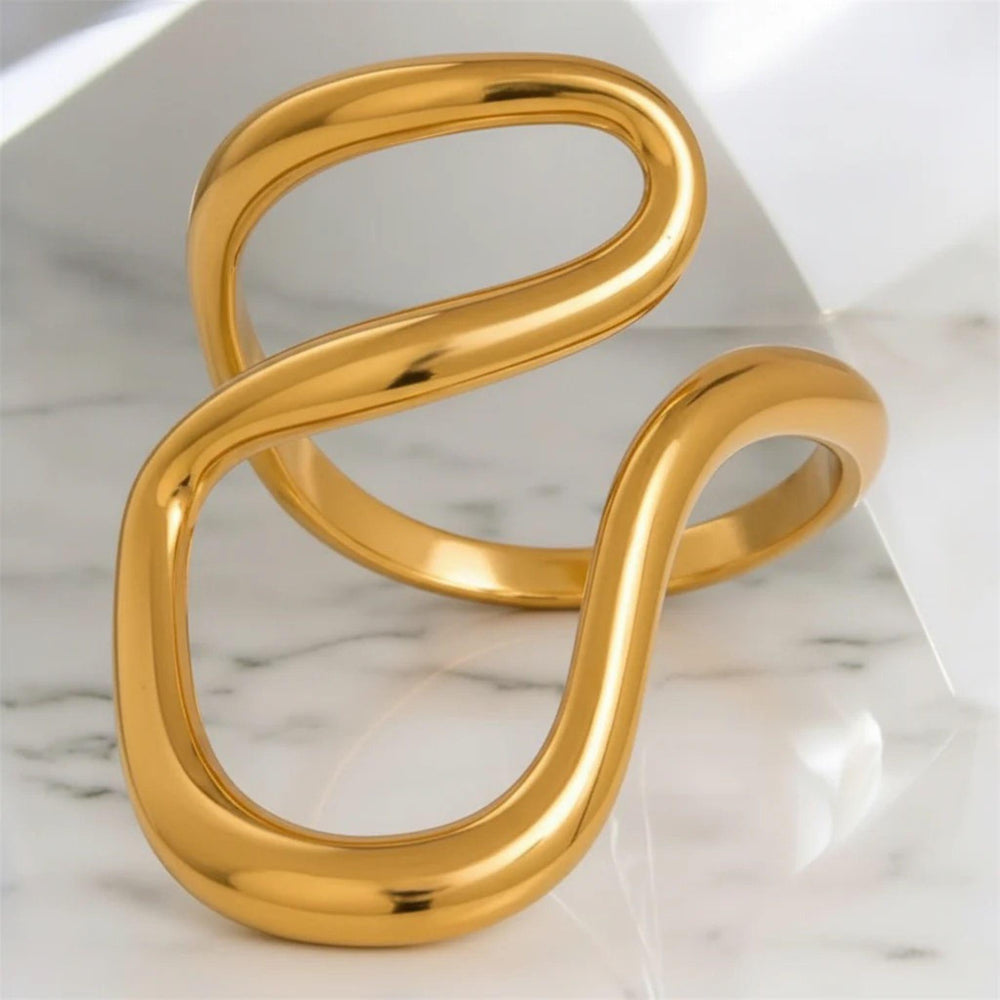 Eleganter goldfarbener Wellenring mit skulpturaler, offener Form – moderner Statement-Ring von LOÉAR auf hellem Hintergrund.