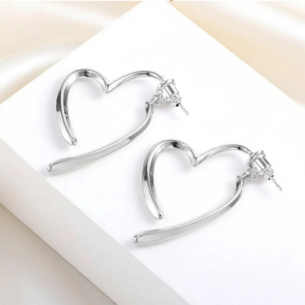 Silberne, offen geformte Herz-Ohrringe mit fließender Linienführung auf hellem Hintergrund.