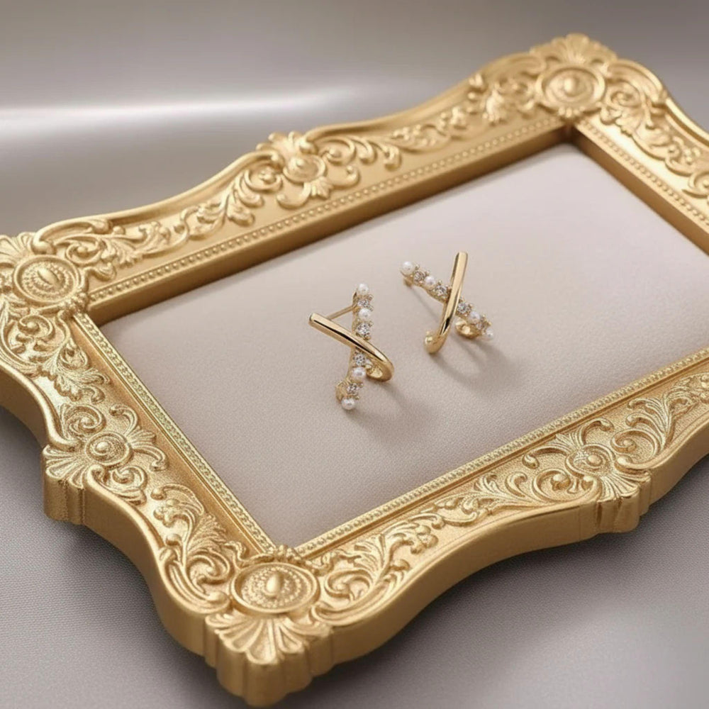 Vergoldete X-Design Ohrringe mit Perlen und Zirkonia auf satinierter Oberfläche.