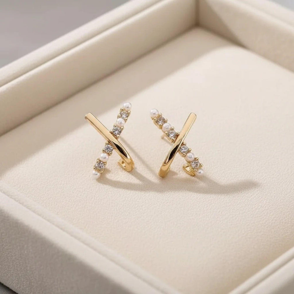 Vergoldete X-Design Ohrringe mit Perlen und Zirkonia auf satinierter Oberfläche.