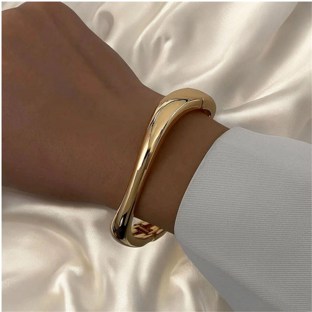 Elegantes Armband in glänzendem Goldton mit fließender, moderner Form – minimalistischer Armreif von LOÉAR, getragen am Handgelenk.